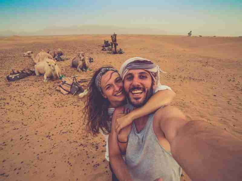 Young couple in love standing near many camels in africa desert taking photo with them, enjoying safari desert